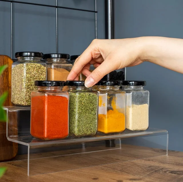 Main atteignant une rangée de pots d'épices colorés dans une cuisine