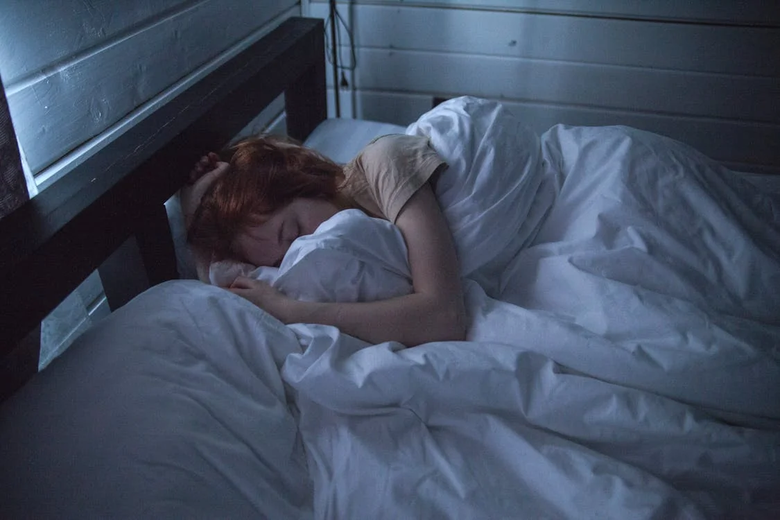 Femme dormant sereinement dans un lit douillet, évoquant l'effet de l'huile essentielle de mandarine.